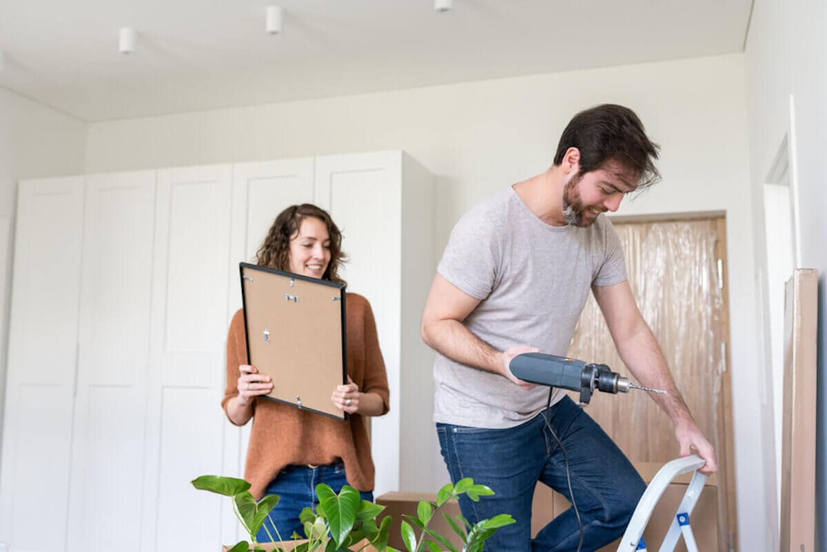 A couple works together to hang a picture frame on the wall of their home.