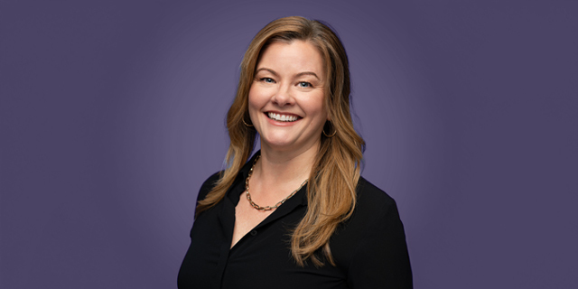 A person smiles while holding a purple flower.